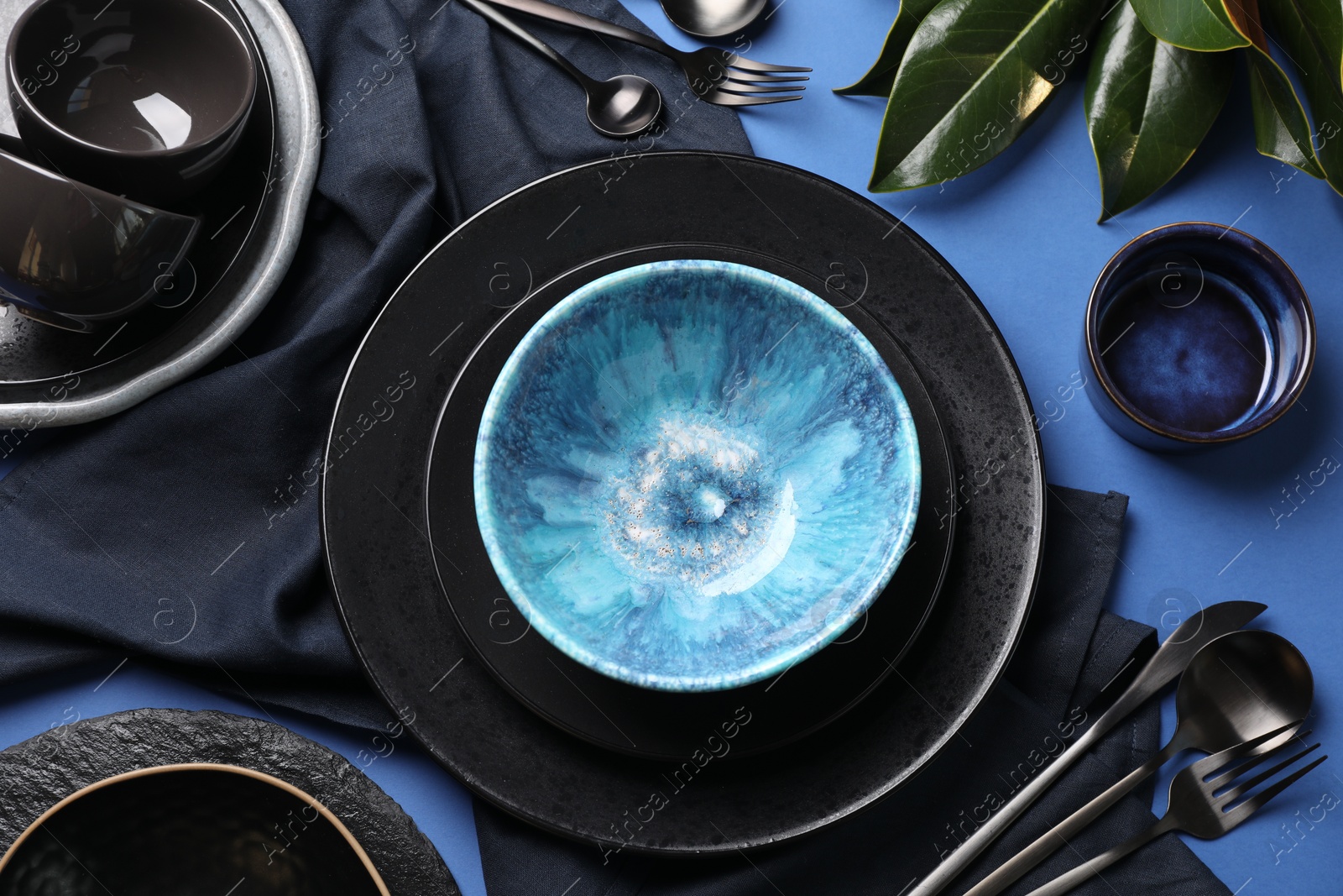 Photo of Stylish table setting. Dishware, cutlery and floral decor on blue background, flat lay