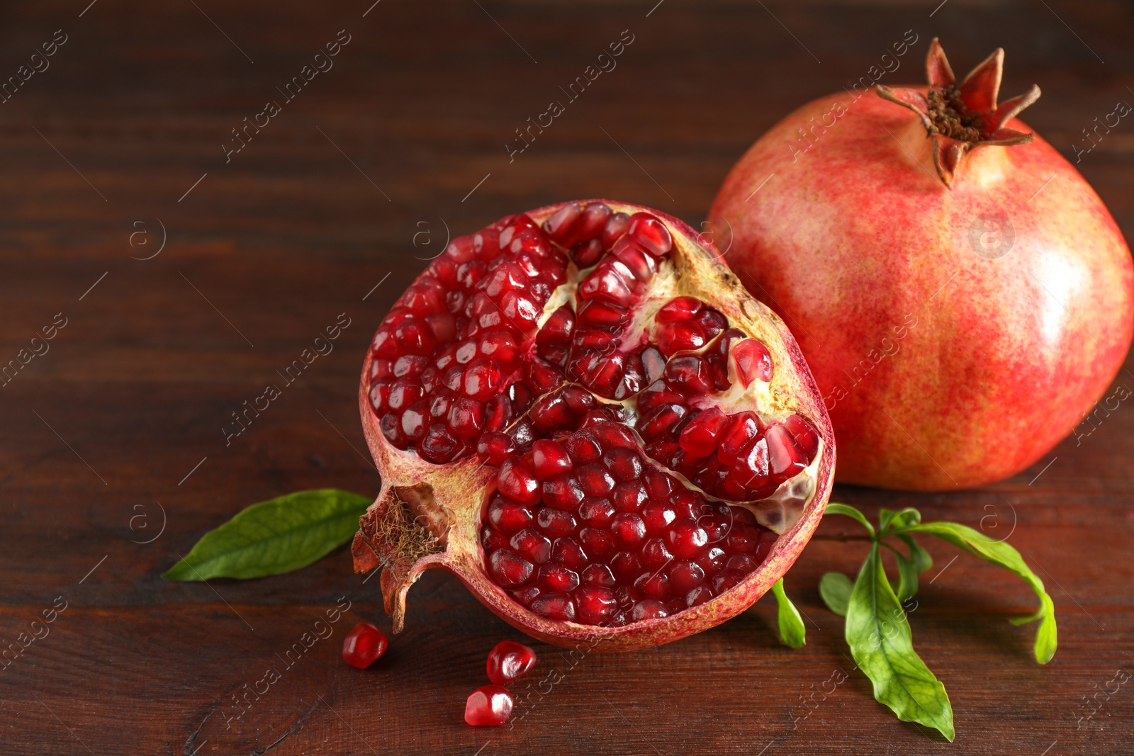 Photo of Fresh pomegranates and green leaves on wooden table, closeup