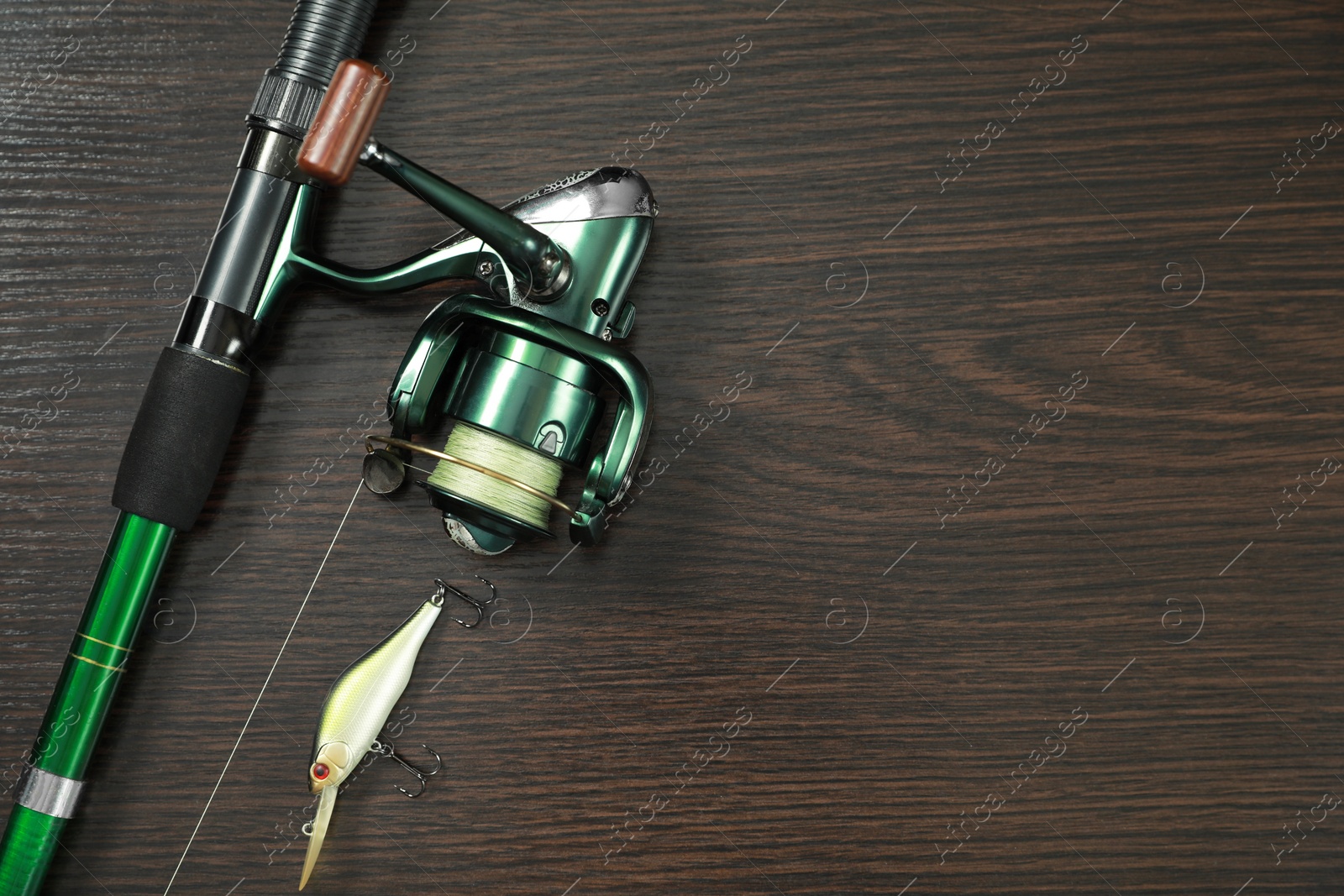 Photo of Fishing rod with reel and lure on dark wooden background, top view. Space for text