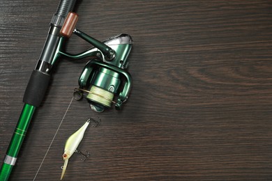 Photo of Fishing rod with reel and lure on dark wooden background, top view. Space for text