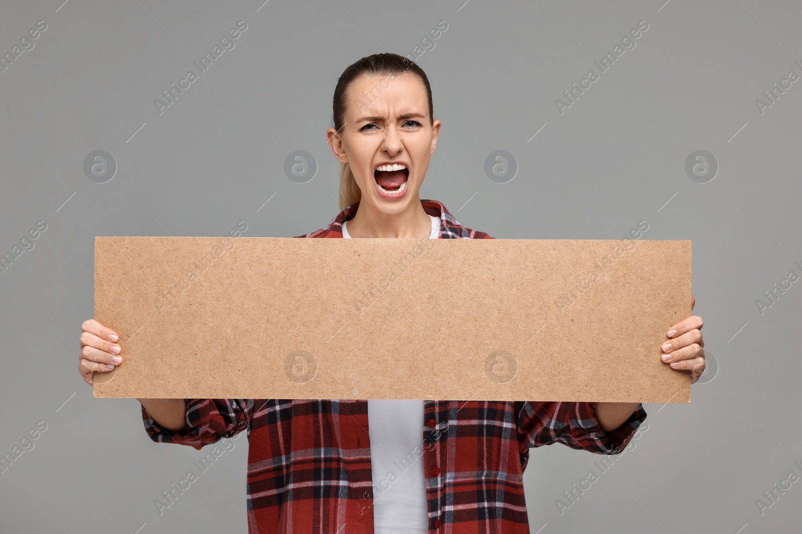 Photo of Emotional woman holding blank cardboard banner on grey background, space for text