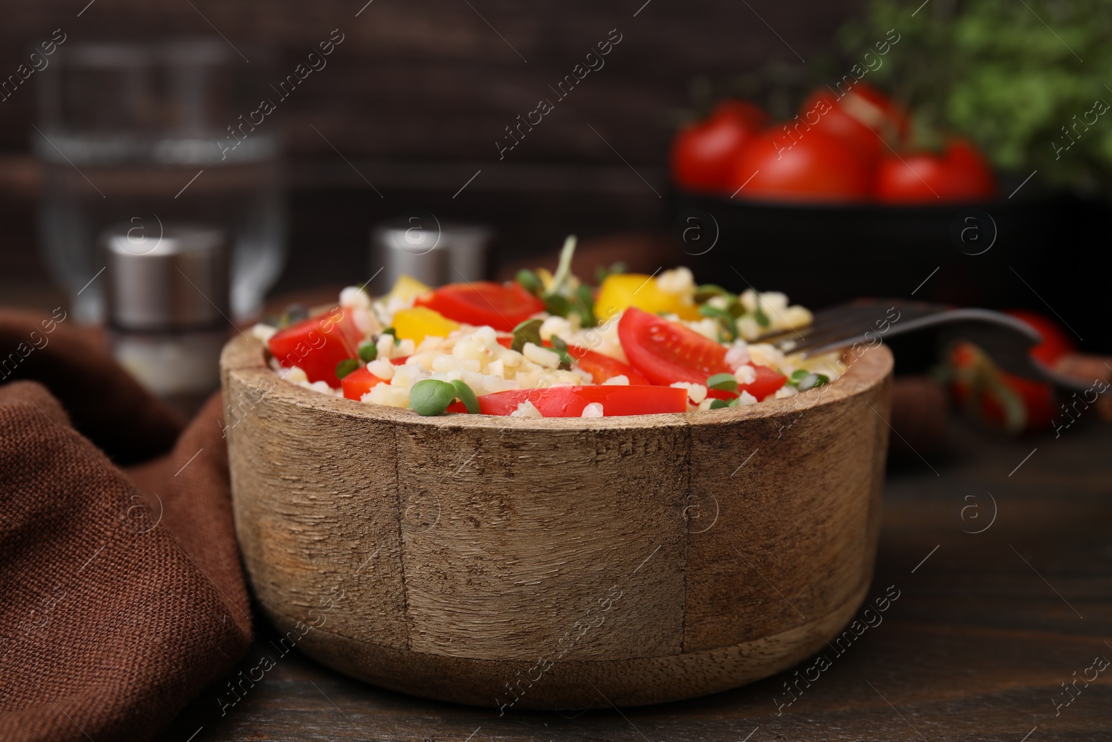 Photo of Cooked bulgur with vegetables in bowl on wooden table, closeup