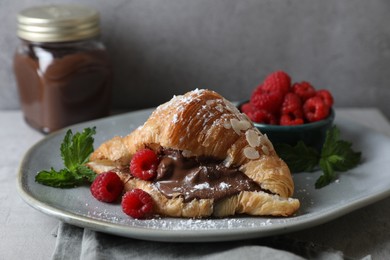 Photo of Delicious croissant with chocolate and raspberries on grey table, closeup