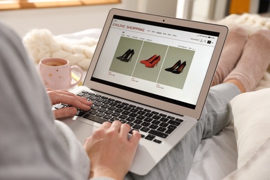 Photo of Woman using laptop for online shopping indoors, closeup