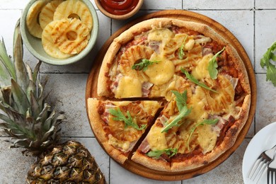 Photo of Delicious cut pineapple pizza and ingredients on light gray tiled table, flat lay