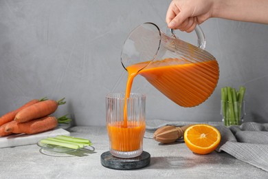 Photo of Woman pouring carrot juice from jug into glass at light grey table, closeup