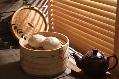 Photo of Delicious Chinese steamed buns and kettle on wooden table, closeup