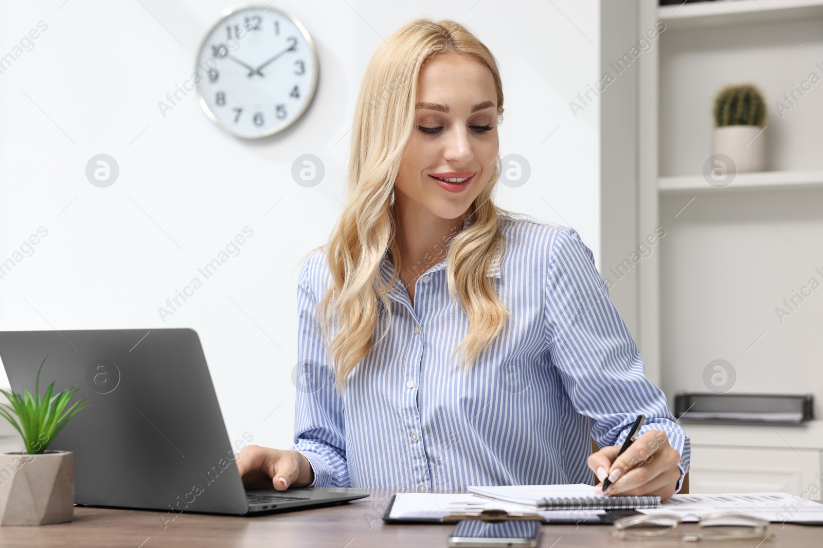 Photo of Happy secretary taking notes at table in office