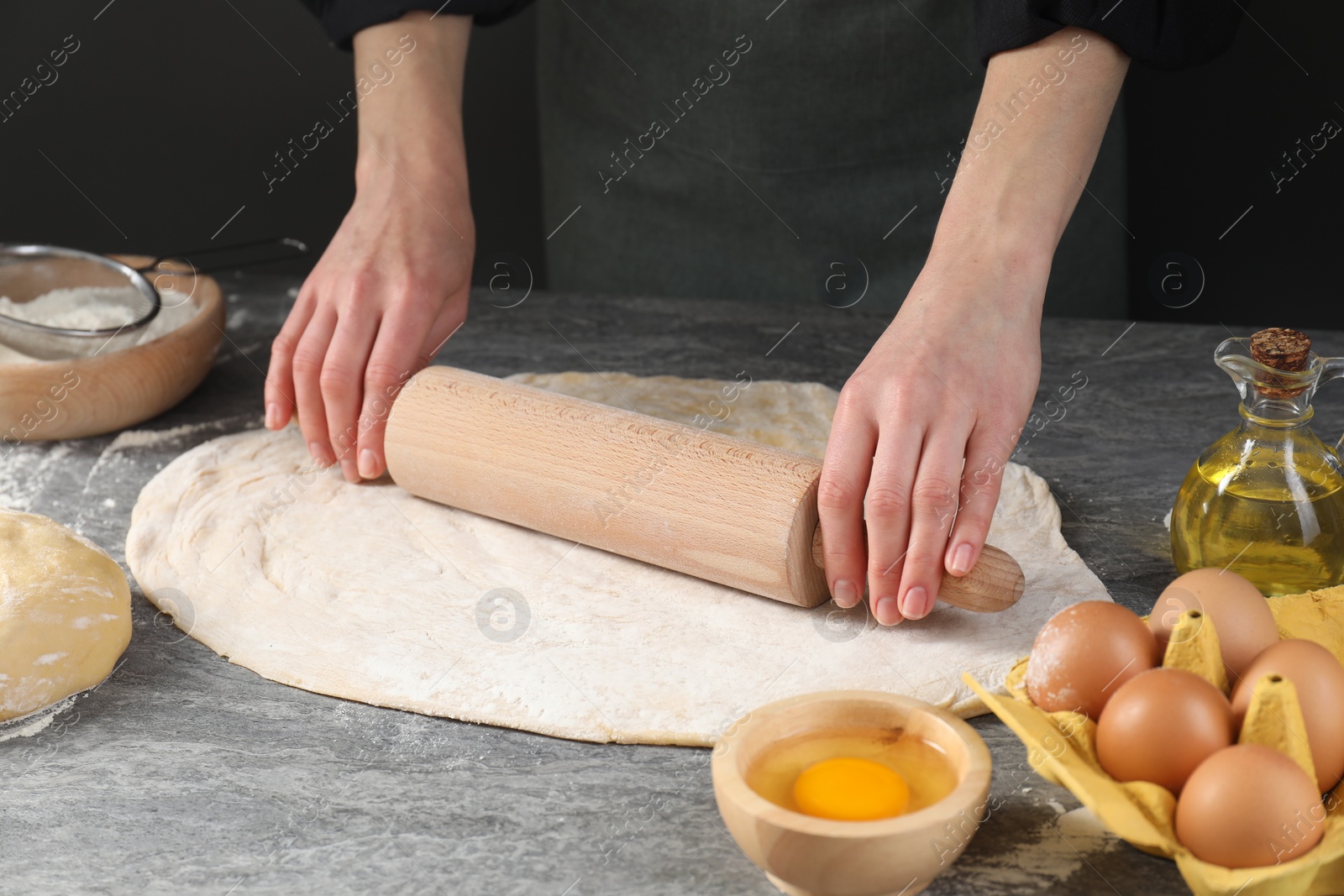 Photo of Woman rolling raw dough at grey table, closeup