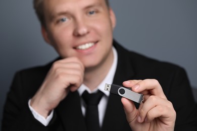 Photo of Man with usb flash drive against grey background, focus on device. Space for text