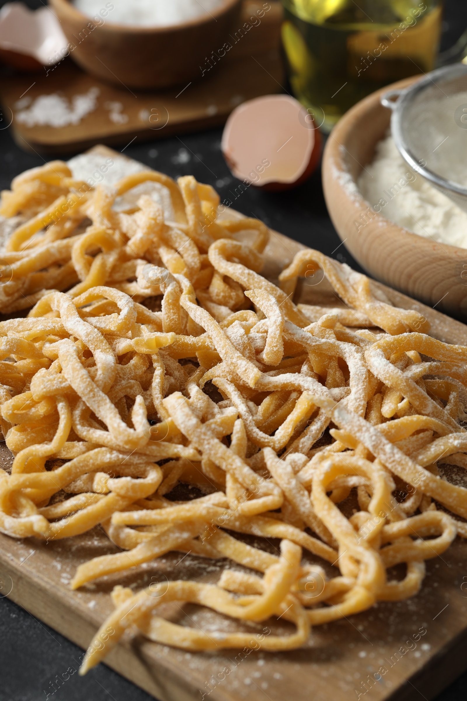 Photo of Board with homemade pasta, flour and ingredients on dark table, closeup