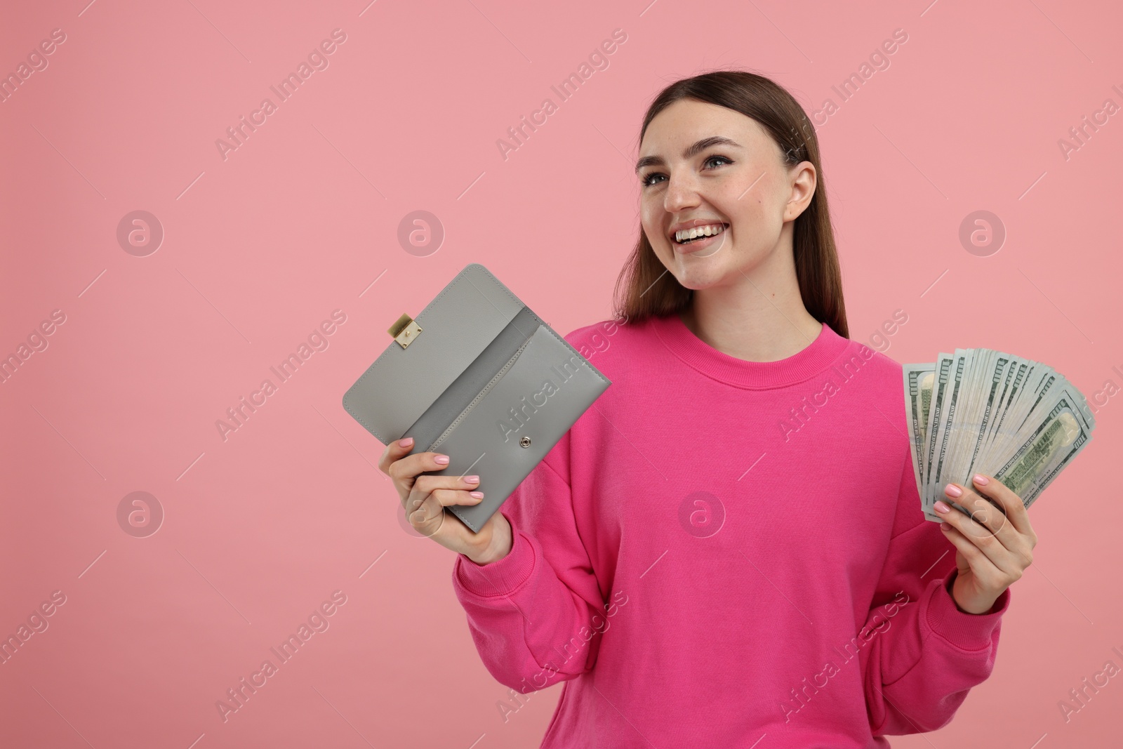 Photo of Happy woman with wallet and dollar banknotes on pink background, space for text