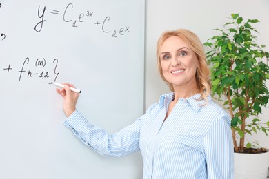 Professor writing down math equation on whiteboard indoors