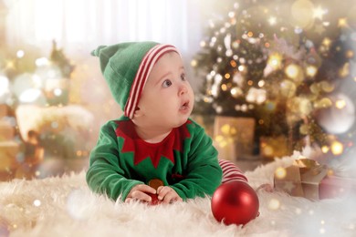 Image of Baby wearing cute elf costume on floor in room decorated for Christmas. Magical festive atmosphere