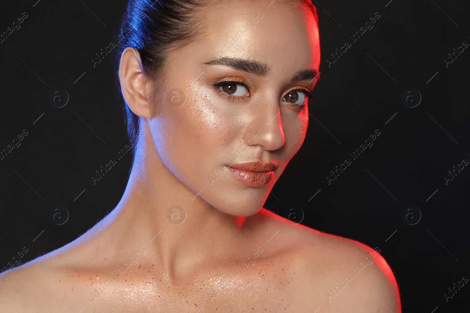 Photo of Beautiful young woman with glitter makeup on black background