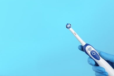 Photo of Dentist holding electric toothbrush on color background, space for text