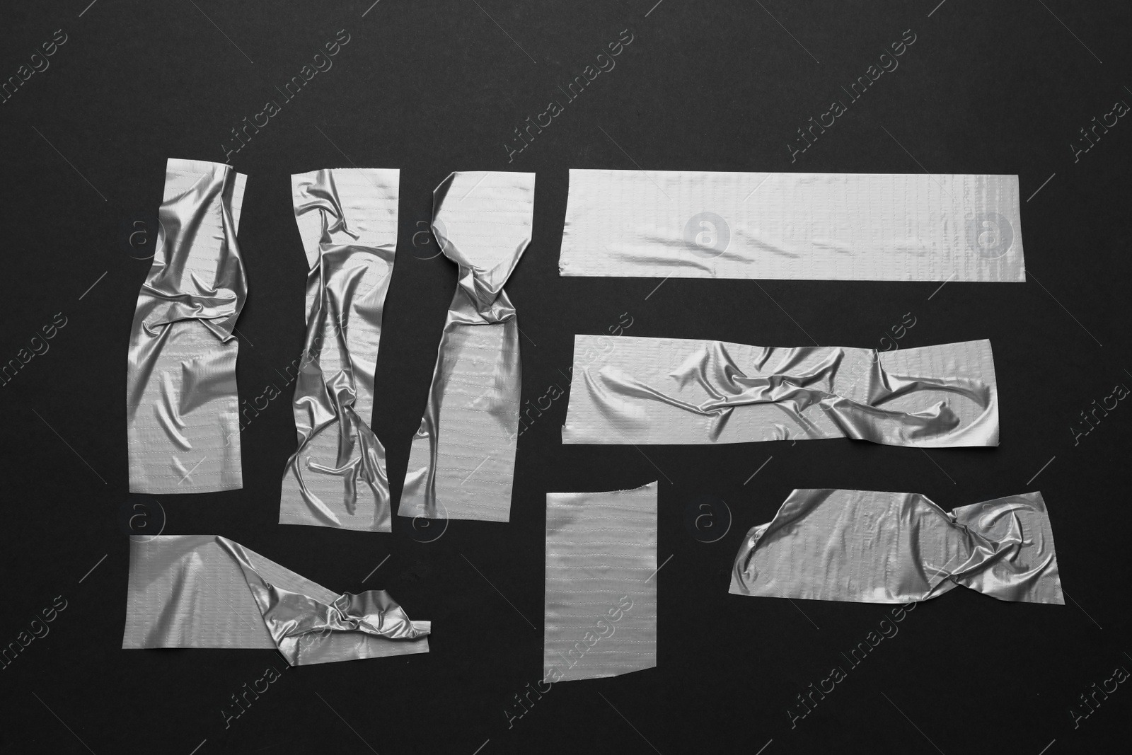 Photo of Many pieces of silver adhesive tape on black background, flat lay