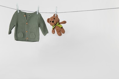 Baby shirt and toy bear drying on laundry line against light background
