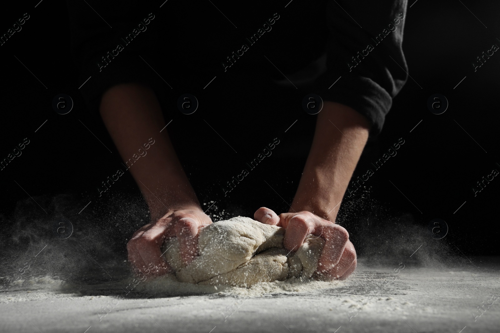 Photo of Making bread. Woman kneading dough at table on dark background, closeup