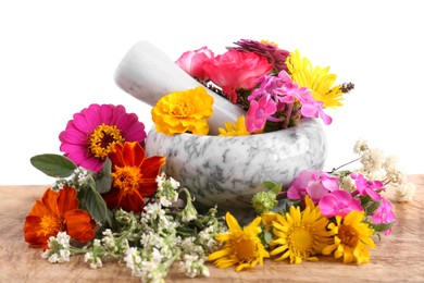 Marble mortar, pestle and different flowers on wooden table against white background