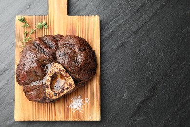 Photo of Piece of delicious grilled beef meat, thyme and salt on black table, top view. Space for text