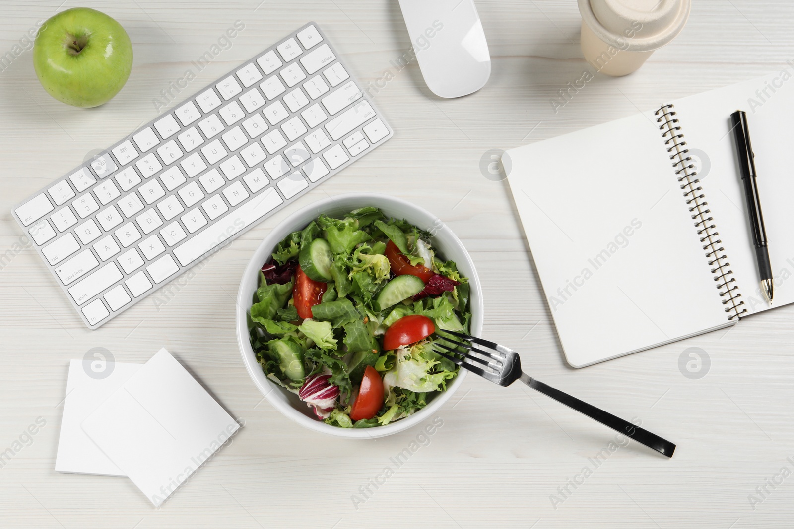 Photo of Bowl of tasty food, keyboard, fork, apple and notebook on white wooden table, flat lay. Business lunch