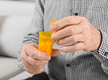 Photo of Senior man holding bottle of pills indoors, closeup