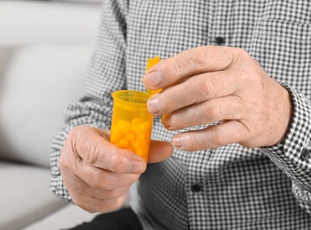 Senior man holding bottle of pills indoors, closeup