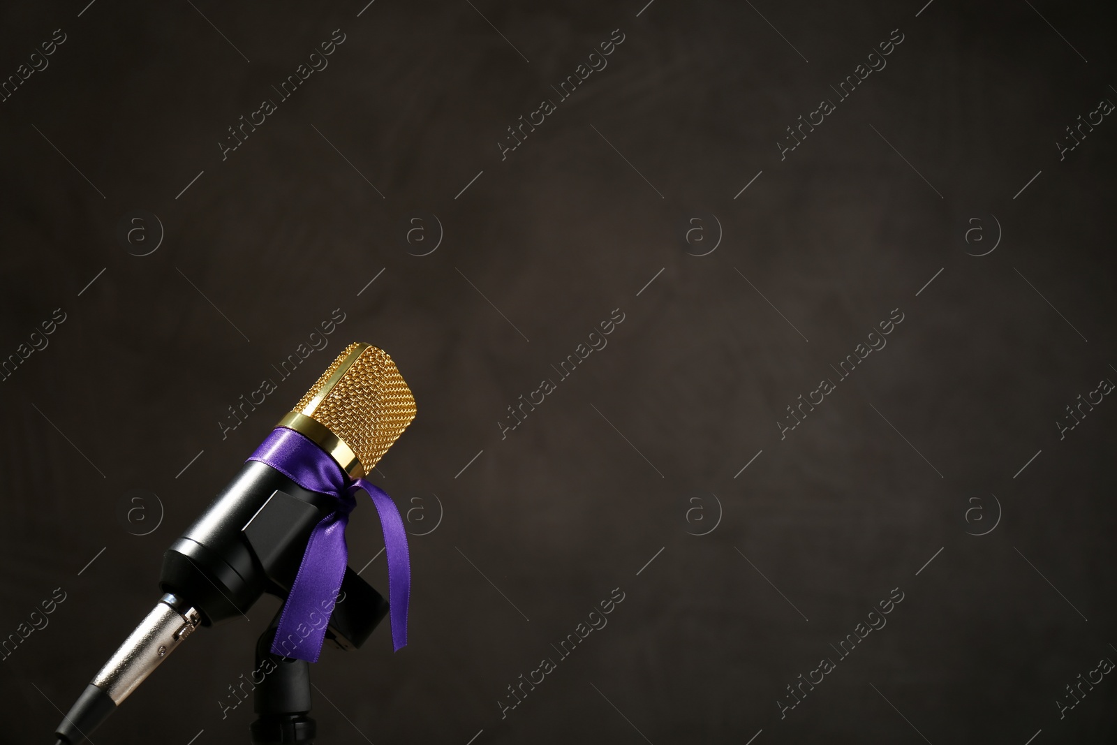 Photo of Microphone with purple awareness ribbon on dark background, space for text