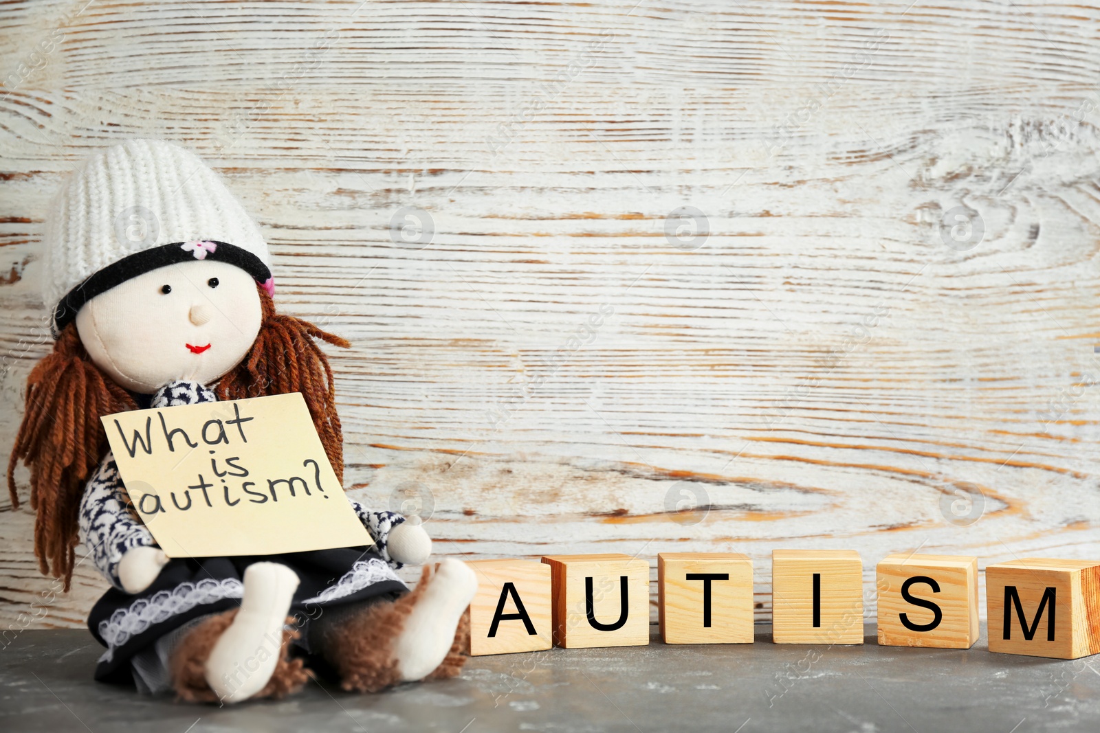 Photo of Doll holding note with phrase "What is autism?" and cubes on table
