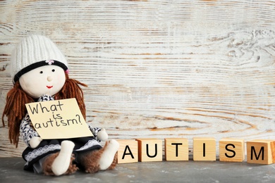 Doll holding note with phrase "What is autism?" and cubes on table