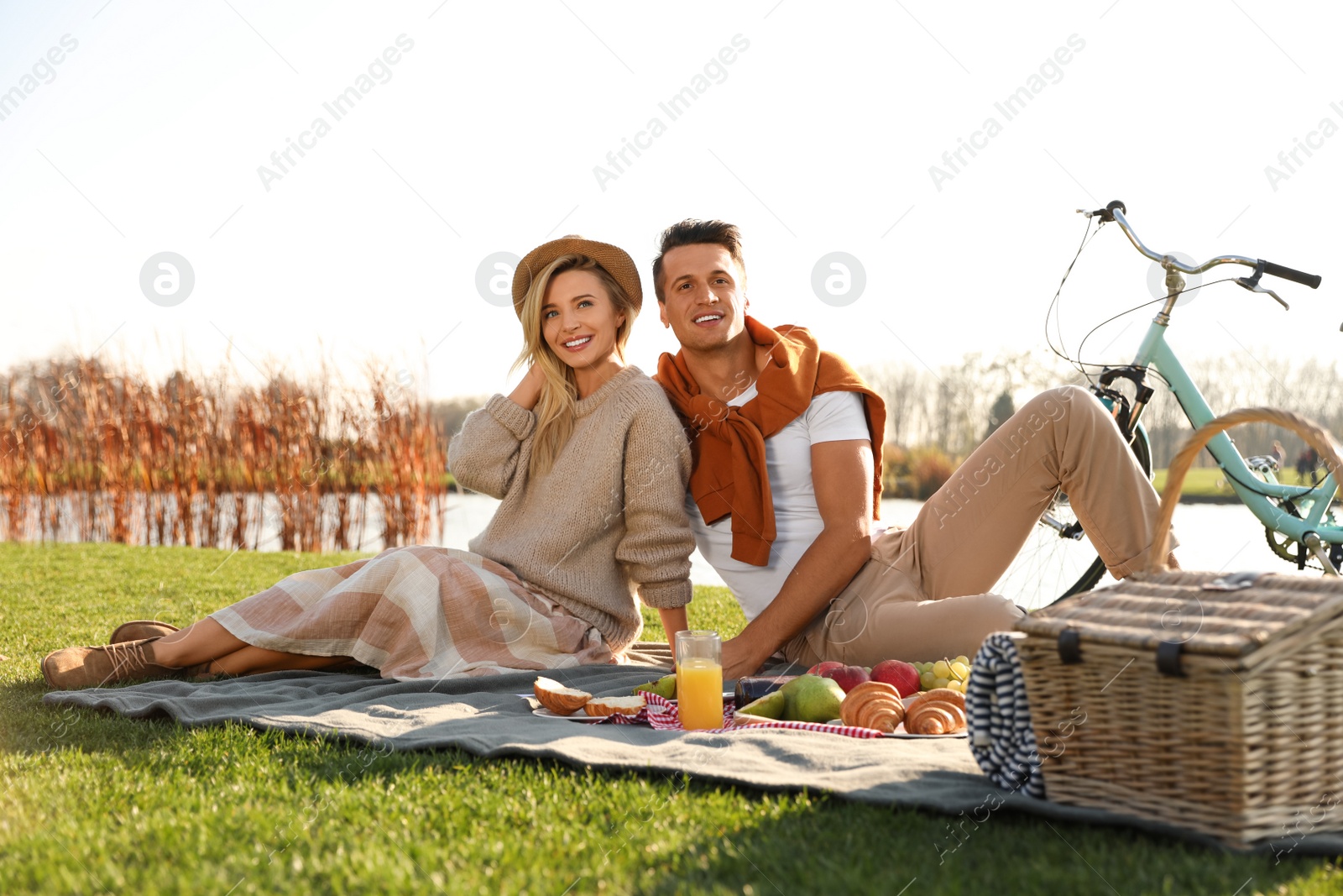 Photo of Happy young couple having picnic near lake on sunny day