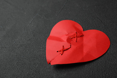 Photo of Torn paper heart sewed with thread on black stone background. Relationship problems concept