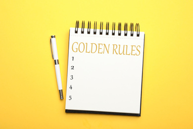 Image of Stylish open notebook with phrase GOLDEN RULES and pen on yellow background, top view