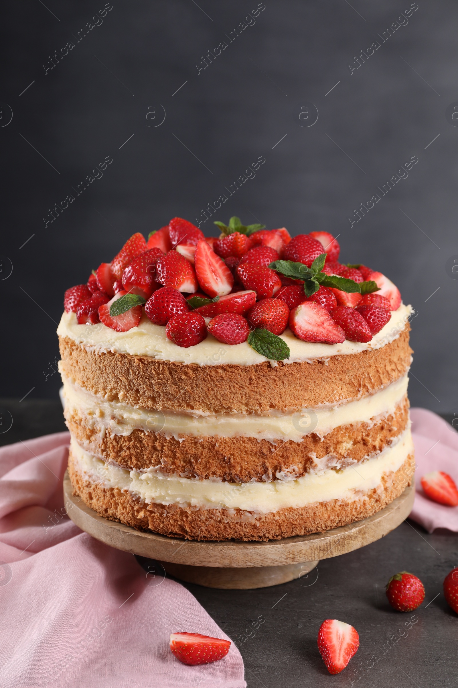 Photo of Tasty cake with fresh strawberries and mint on table against dark gray background