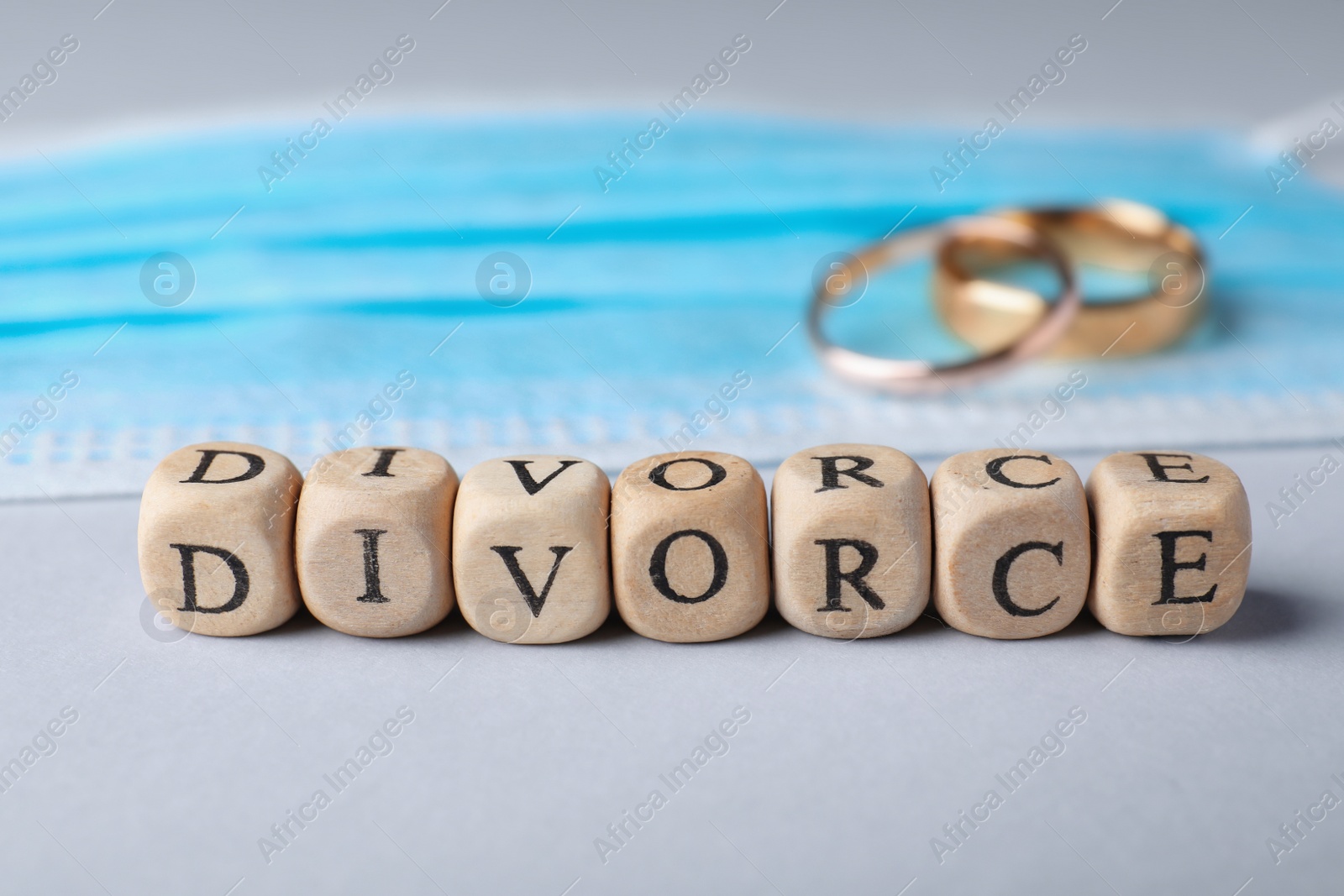 Photo of Wooden cubes with word Divorce, wedding rings and medical mask on grey background. Breaking family ties during coronavirus outbreak