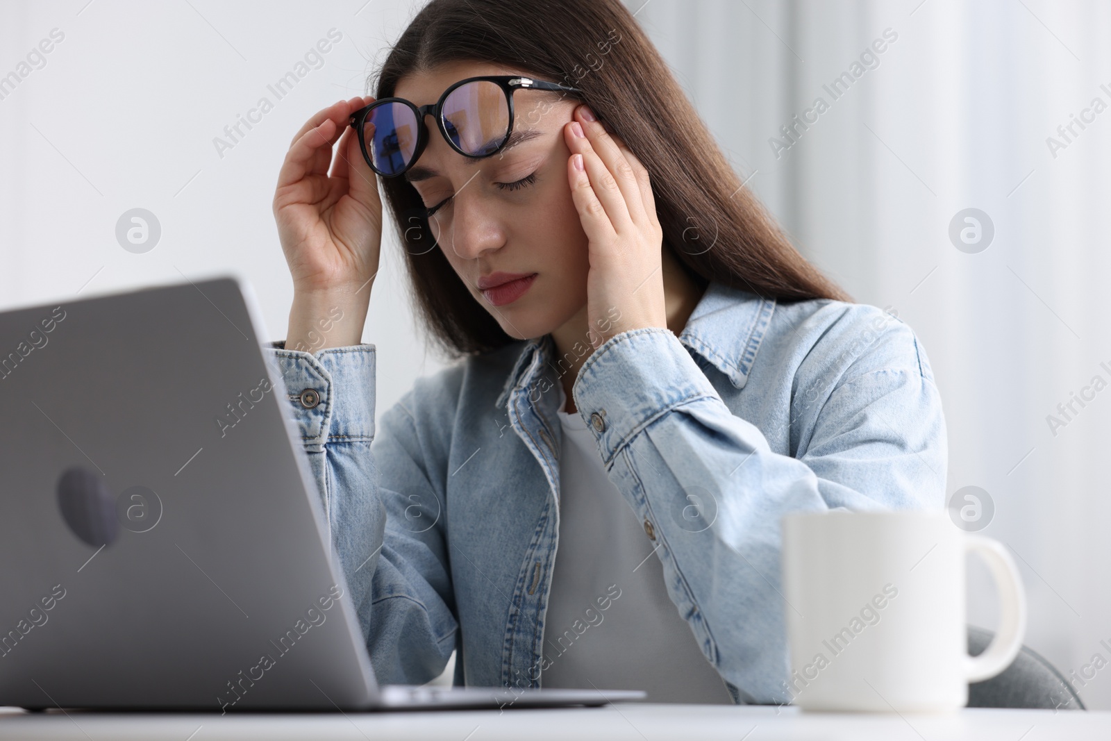 Photo of Woman with glasses suffering from headache at workplace in office