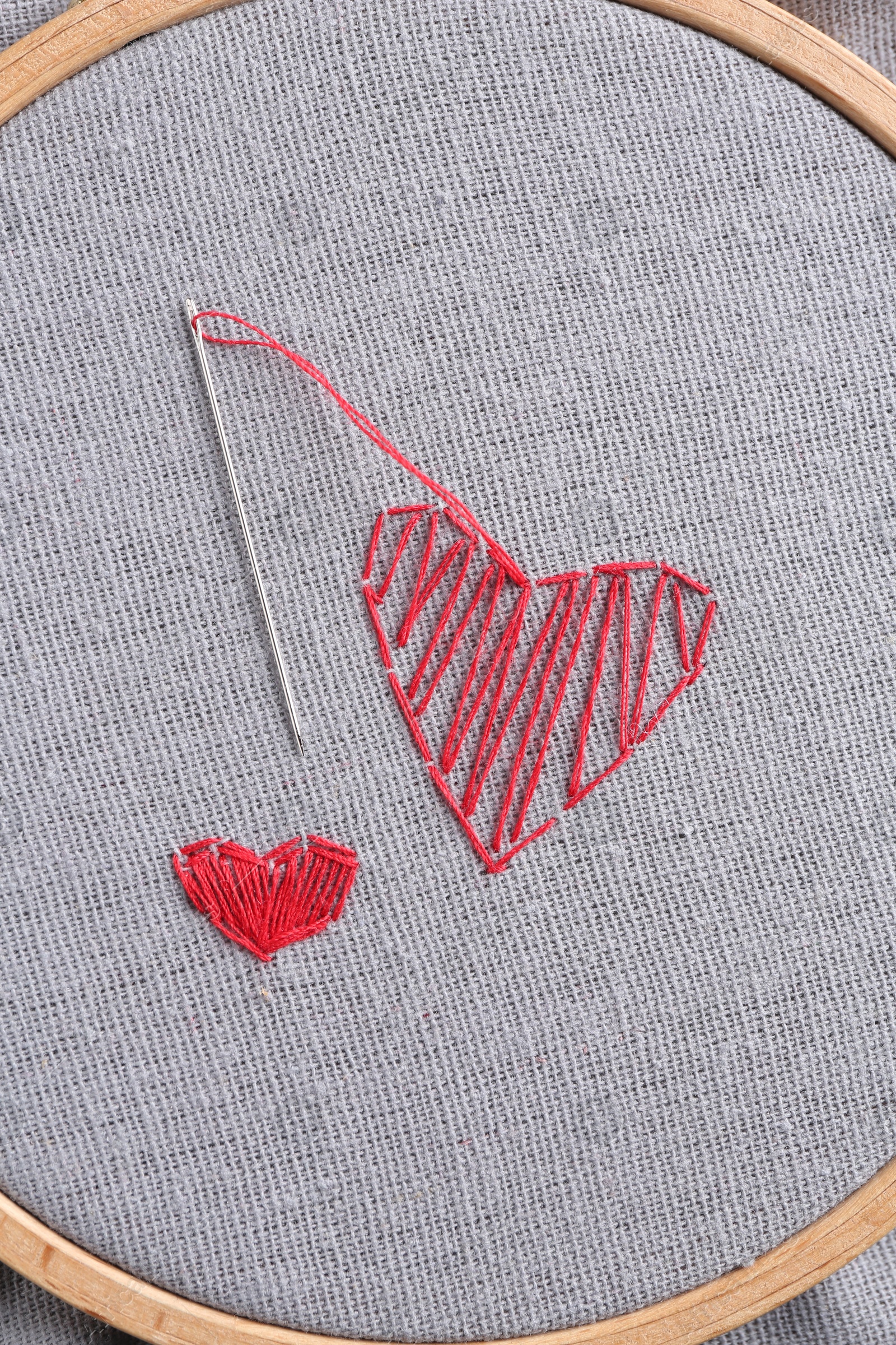 Photo of Embroidered red hearts and needle on light grey cloth, top view
