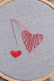 Embroidered red hearts and needle on light grey cloth, top view