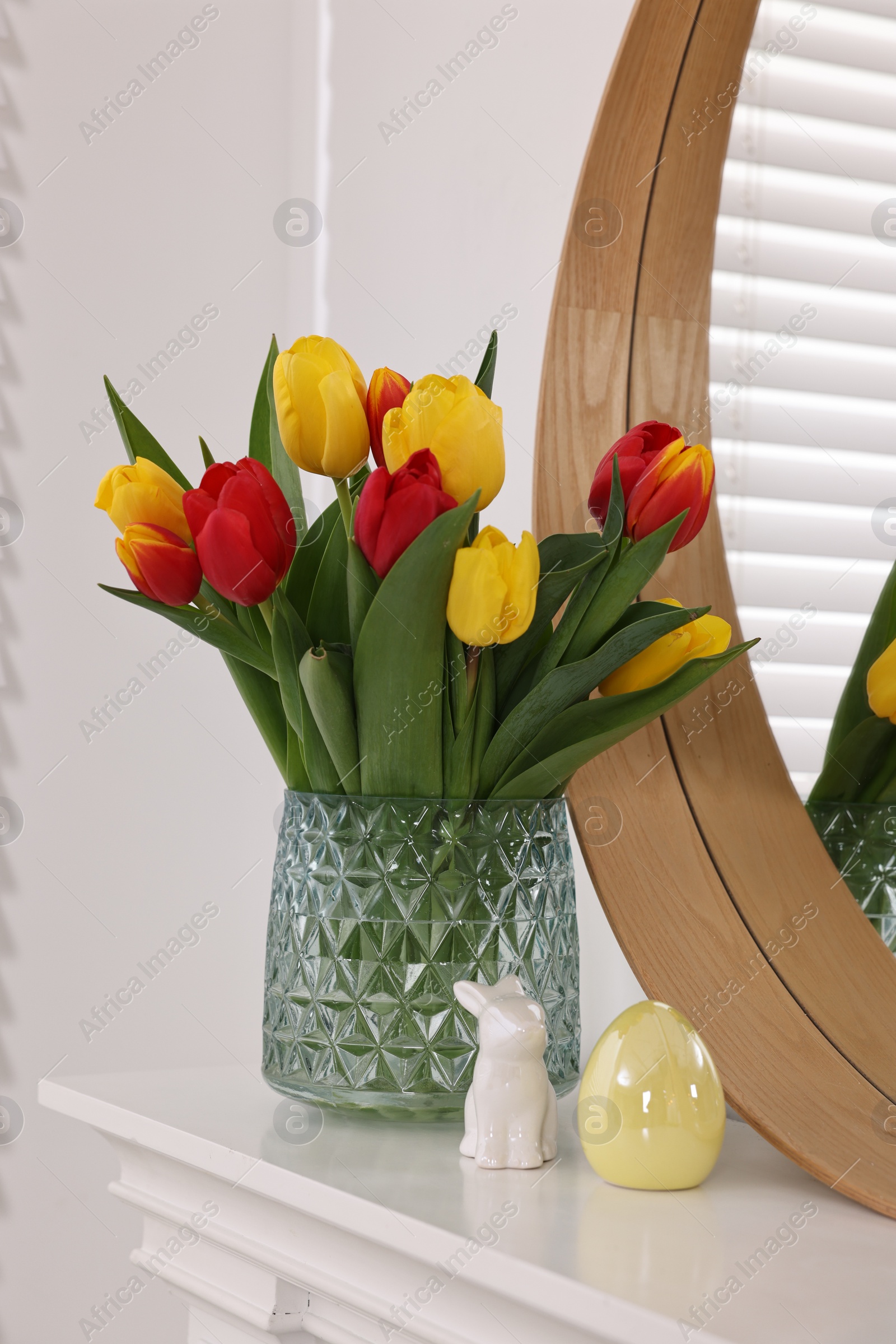 Photo of Easter decorations. Bouquet of tulips in vase and figures on fireplace at home