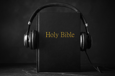 Photo of Bible and headphones on black background. Religious audiobook