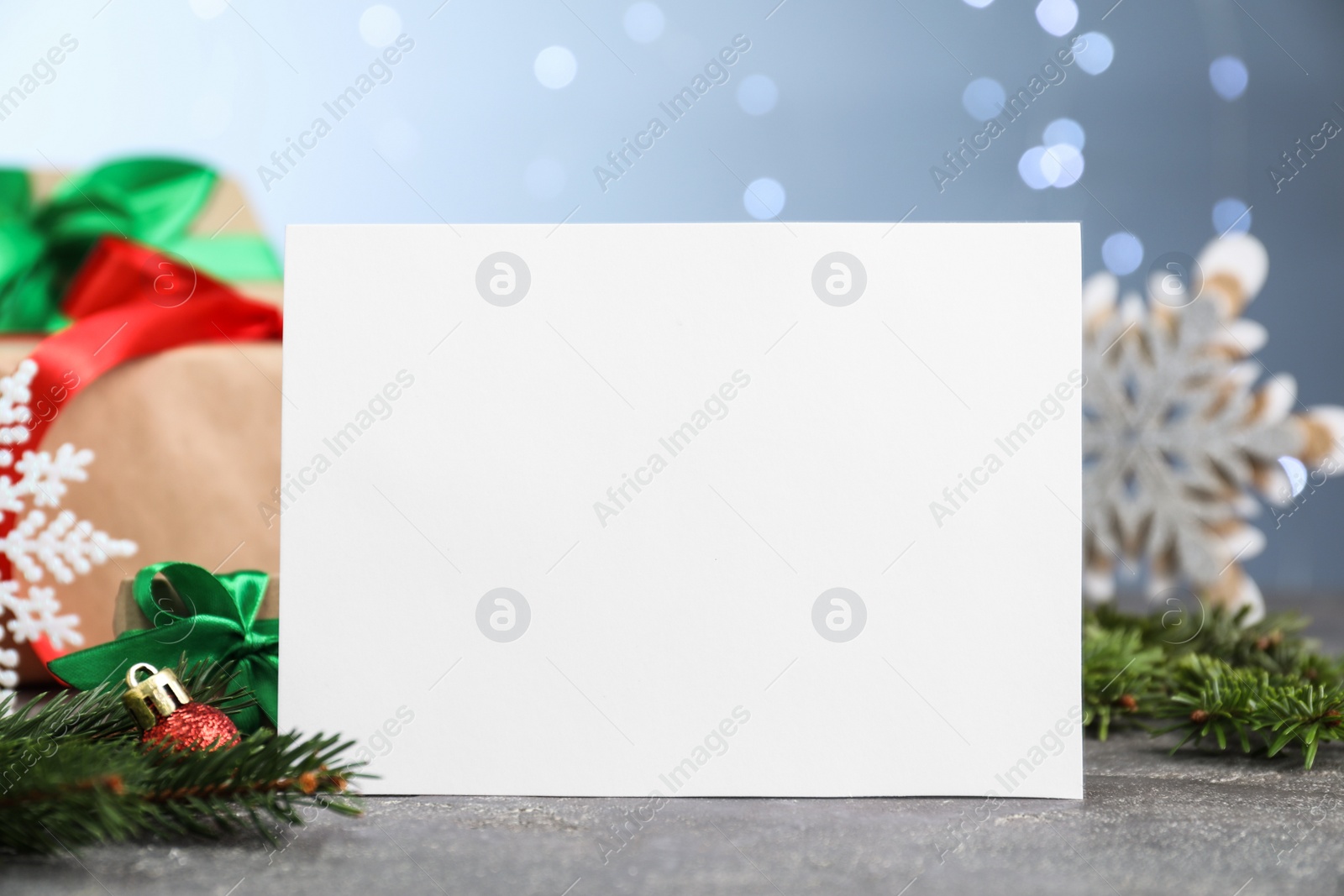 Photo of Blank card Christmas and festive decor on grey table against blurred lights, closeup. Space for text