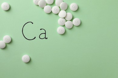 Photo of Flat lay composition with calcium supplement pills on light green background, space for text
