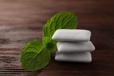 Photo of Tasty white chewing gums and mint leaves on wooden table, closeup