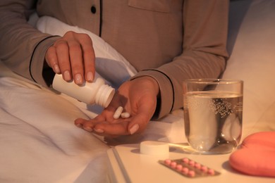 Photo of Woman pouring pills from bottle into hand indoors, closeup. Insomnia treatment
