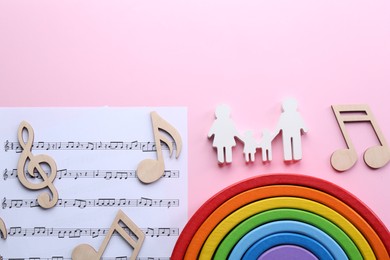 Baby songs. Music sheet, figures of family, wooden notes and toy rainbow on pink background, flat lay