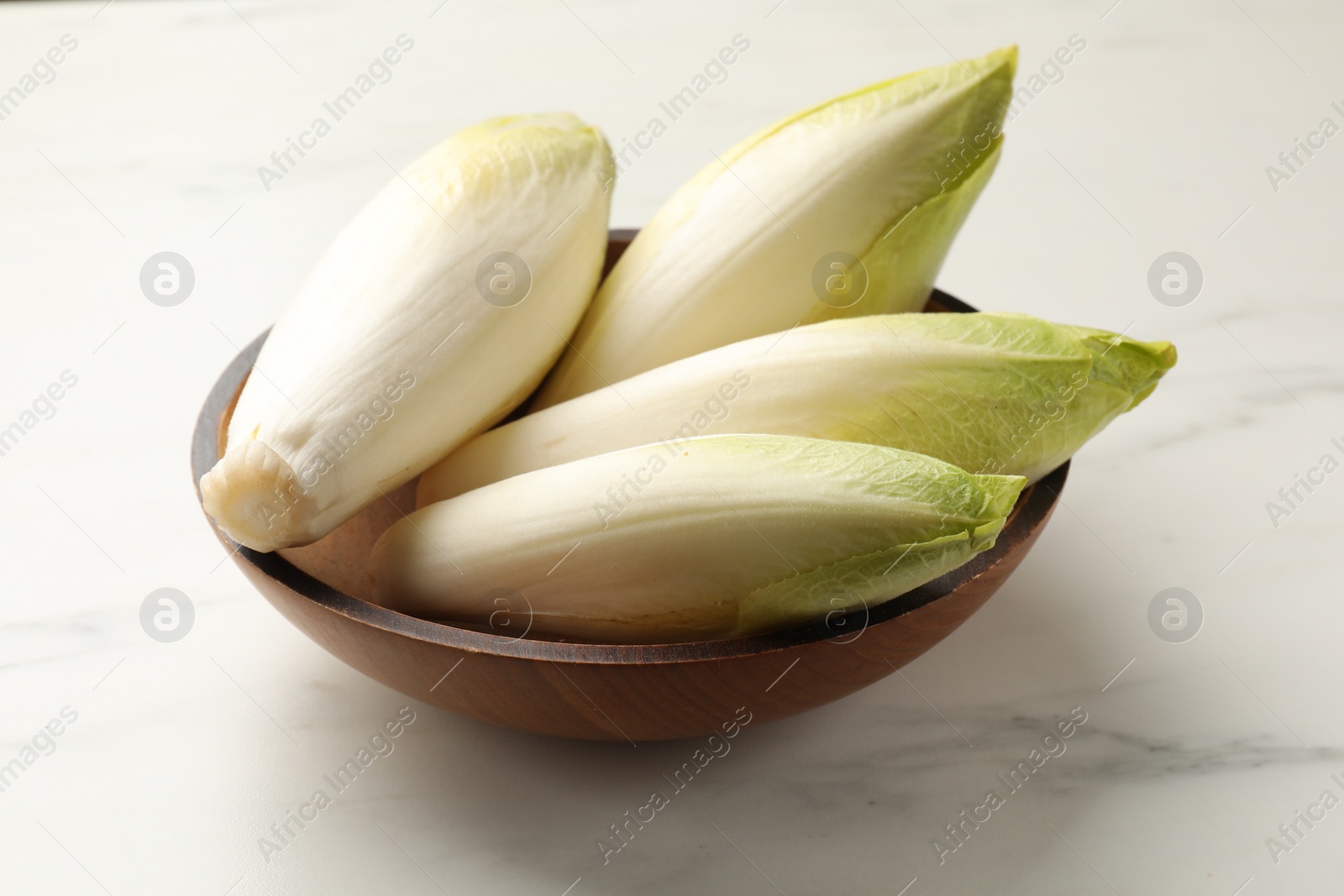 Photo of Raw ripe chicories in bowl on white marble table, closeup