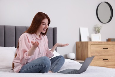 Happy woman having video chat via laptop on bed in bedroom