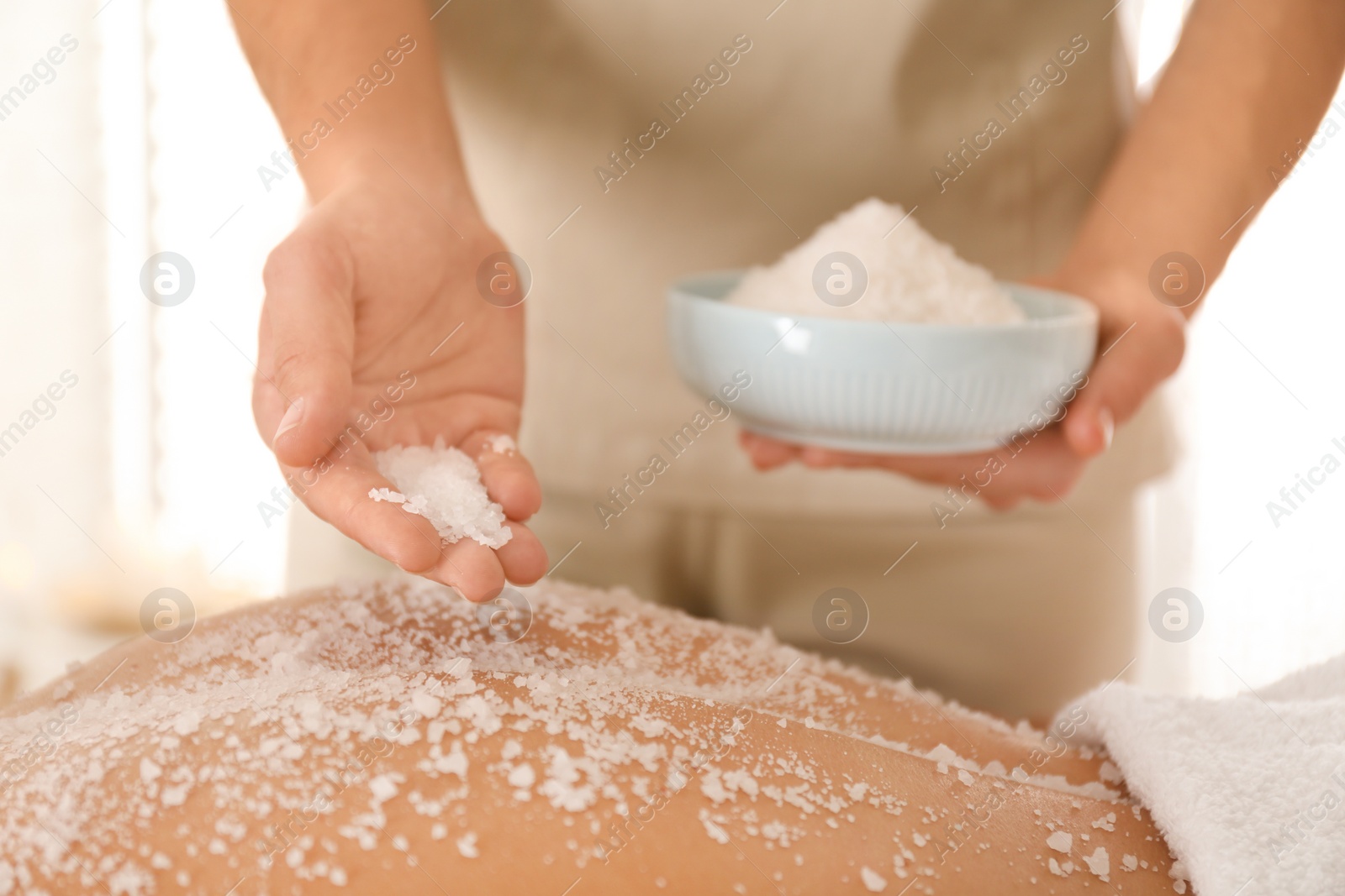 Photo of Young woman having body scrubbing procedure with sea salt in spa salon, closeup