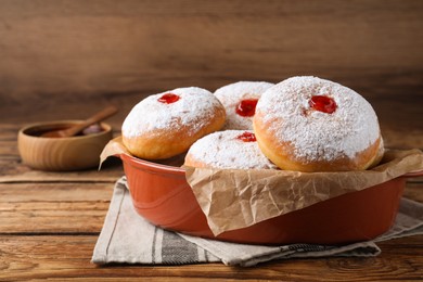 Photo of Delicious donuts with jelly and powdered sugar in baking dish on wooden table